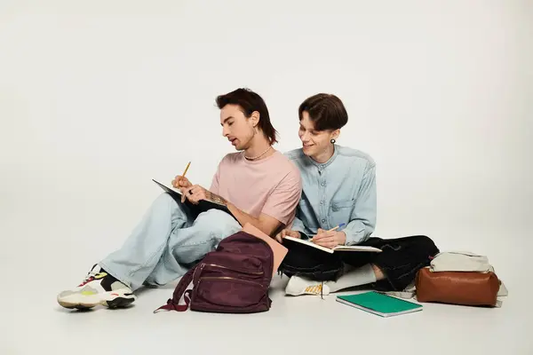 stock image Two young students, dressed casually, sit on a white background while studying together.