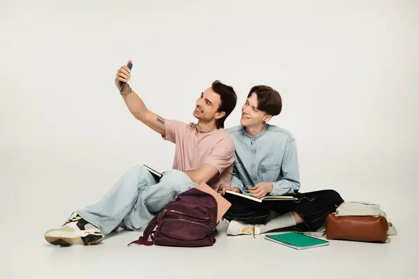 stock image Two young students sit on a grey background taking a selfie.