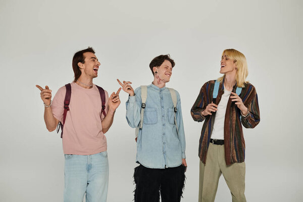 Three young queer students laugh and point while standing against a white backdrop.