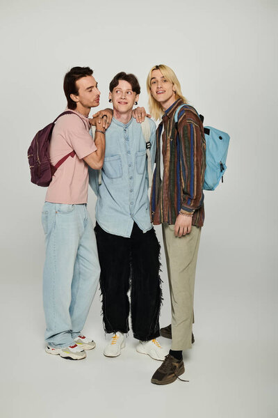 Three young people, members of the LGBTQIA community, stand together in casual attire against a grey background.