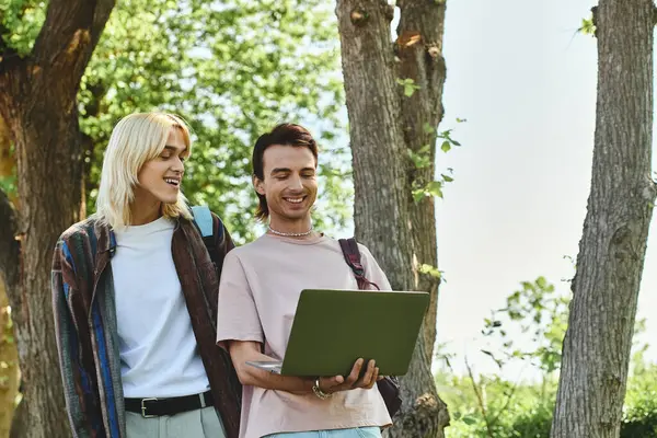 stock image Two young friends, dressed casually, walk through a wooded area. One is holding a laptop.