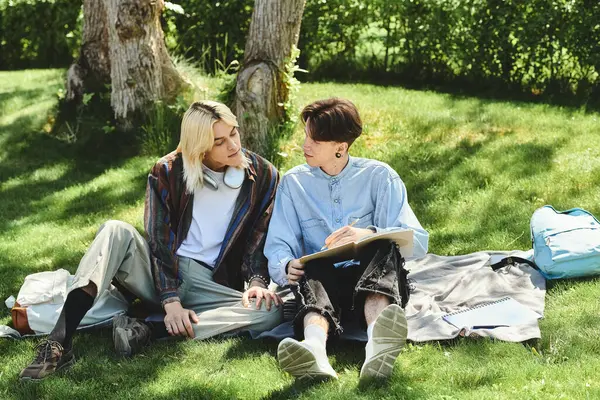 stock image Two young people in casual clothing are sitting on a blanket in the park, talking and smiling.