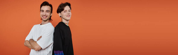 Два молодых друга стоят спиной к спине, ярко улыбаясь на ярком оранжевом фоне.