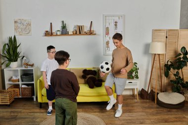 Üç çocuk bir oturma odasında futbol oynuyor..