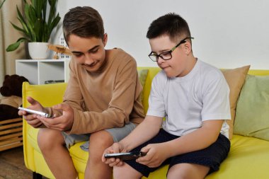 Biri Down sendromlu iki çocuk sarı bir kanepede otururken telefonlarıyla oyun oynuyorlar..