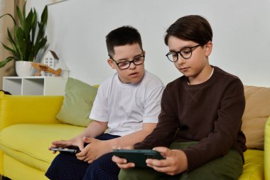 Two boys sit on a yellow couch, one looking at a phone. clipart