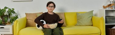 Evde patlamış mısır ve futbol topuyla film izleyen bir çocuk..