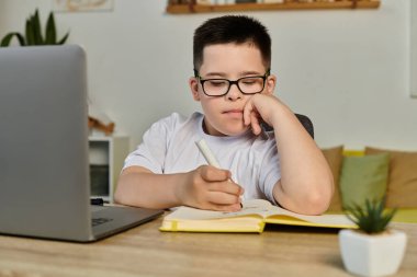 A young boy with Down syndrome concentrates on his schoolwork at home. clipart