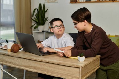 Two young boys, one with Down syndrome, work together on a laptop at home. clipart