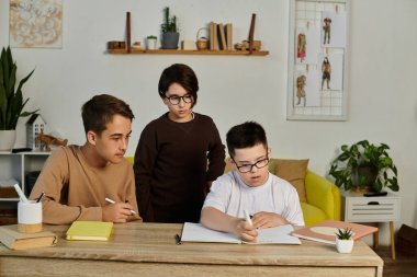 A young boy with Down syndrome writes in his notebook, assisted by his two friends. clipart