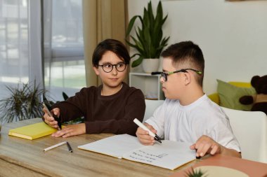 İki çocuk, biri Down sendromlu, bir masada oturup resim çiziyorlar ve etkileşime giriyorlar..