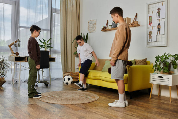 Three young boys play soccer indoors, with one boy juggling the ball.