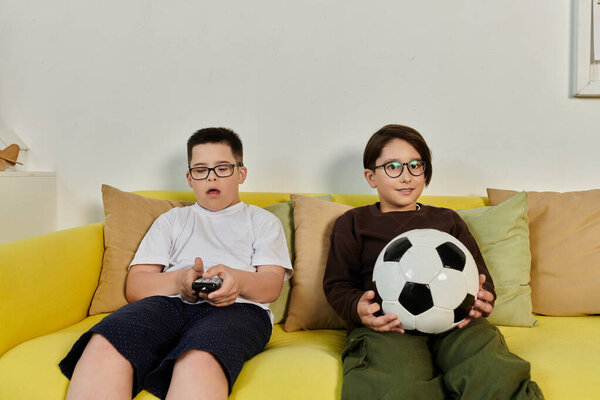 Два мальчика отдыхают на жёлтом диване и смотрят телевизор..