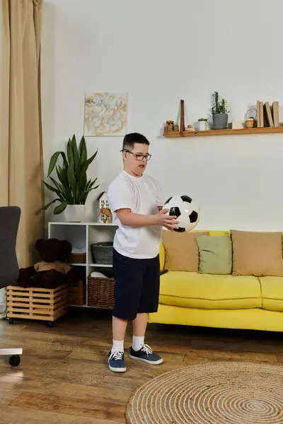 stock image A young boy with Down syndrome holds a soccer ball in his living room.