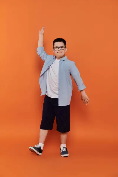 stock image A young boy with Down syndrome stands with a cheerful expression in front of an orange background.