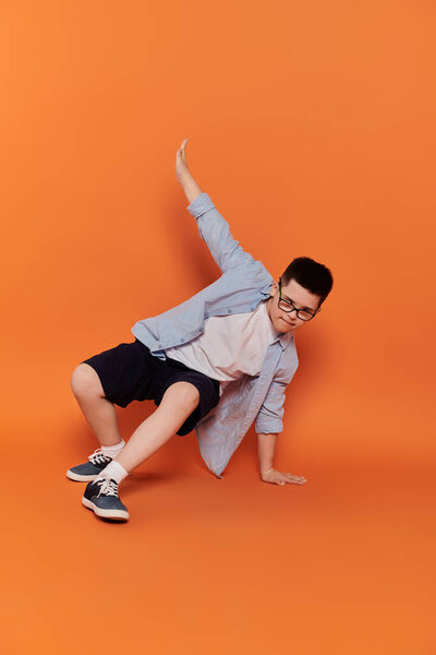 Мальчик с синдромом Дауна танцует брейк-данс перед оранжевым фоном.