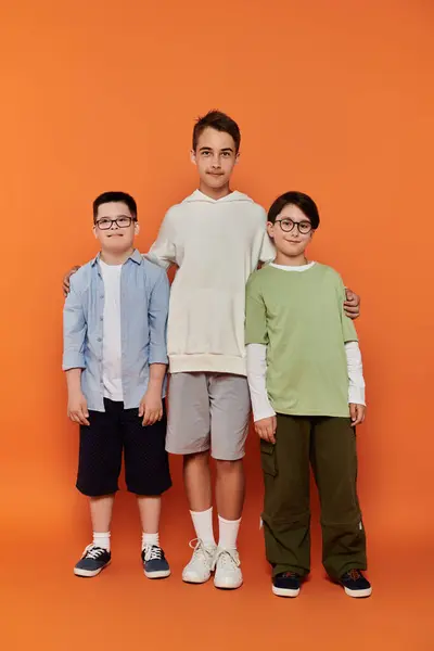 stock image Three young boys stand together in front of an orange background.