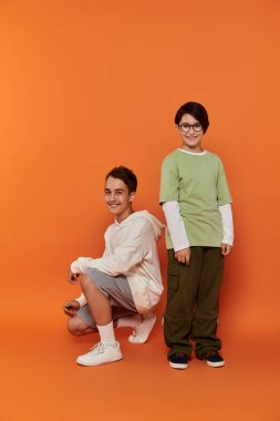 İki çocuk turuncu bir arka planın önünde duruyor..