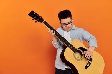 Genç bir çocuk turuncu arka planda gitar çalıyor..
