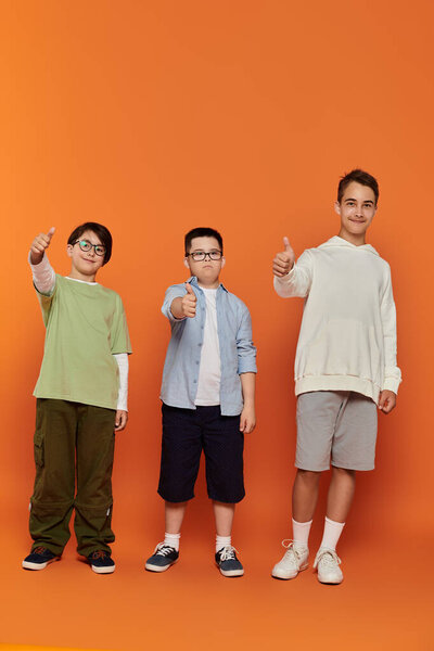 Three boys, including one with Down syndrome, pose for a portrait with thumbs up.