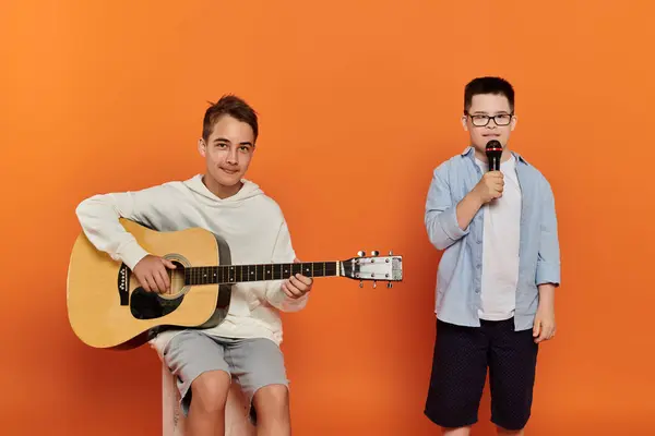 stock image Two young boys, one playing guitar and the other singing into a microphone.