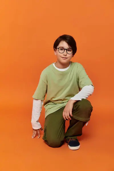 stock image A young boy kneels on an orange background.