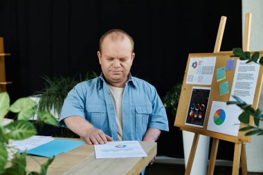 Mavi gömlekli bir adam masasında dosya olan bir kağıdı inceliyor..