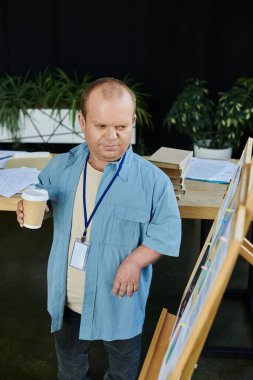 A man with inclusivity stands near a whiteboard, holding a cup of coffee. clipart