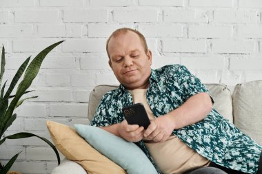 Şablonlu gömleği olan bir adam kanepeye oturmuş, akıllı telefonunu kullanıyor..