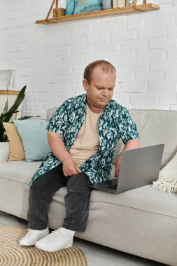 Kapsayıcı bir adam oturma odasındaki bir koltukta oturur ve dizüstü bilgisayarıyla çalışır..