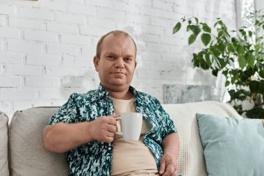 Kapsamlı bir adam bir kanepede oturur, elinde bir fincan, bir ev ortamında.