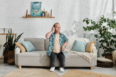 Kapsamlı bir adam, ev ortamında bir kanepede oturur. Etrafı bitkiler ve yastıklarla çevrilidir..