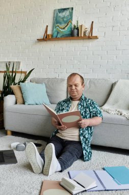 Kapsamlı bir adam yerde oturur, kanepenin önünde kitap okur..