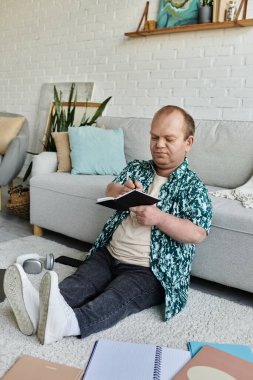 Kapsamlı bir adam yere oturur, bir deftere yazar, rahat, rahat bir ortamda..