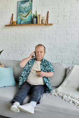 Kapsayıcı bir adam koltukta oturur, telefonla konuşur ve kredi kartı tutar..