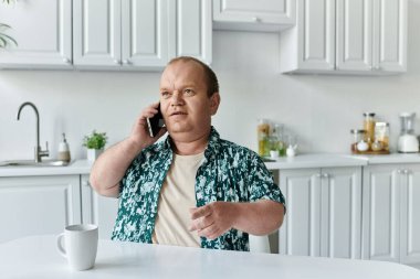 Kapsamlı bir adam mutfak masasında oturup telefonuyla konuşur..