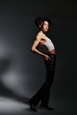 Beyaz askılı genç Afrikalı Amerikalı bir kadın gri bir arka plana karşı poz veriyor..