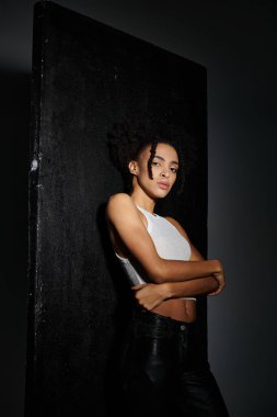 Beyaz askılı şık bir Afro-Amerikalı kadın koyu gri arka plan, moda ve trendlere karşı güvenle poz veriyor..