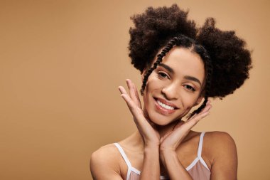 Parlak bir gülüşü ve doğal güzelliği olan genç bir Afrikalı Amerikalı kadın bej arka planda poz veriyor..