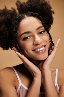 Işıl ışıl parlayan tenli gülümseyen siyah kadın yumuşak ışıkta bej arka planda.