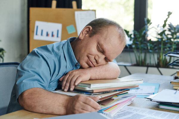 Человек с инклюзивностью дремлет за своим столом, положив голову на стопку бумаг.