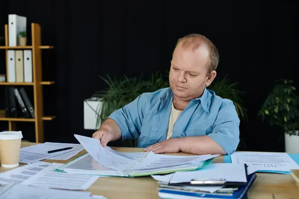 stock image A man with inclusivity sits at a desk, diligently reviewing paperwork.