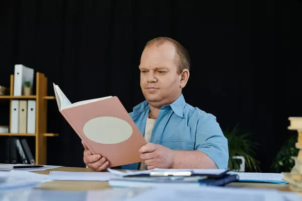 stock image A man with inclusivity sits at a desk reading a book.