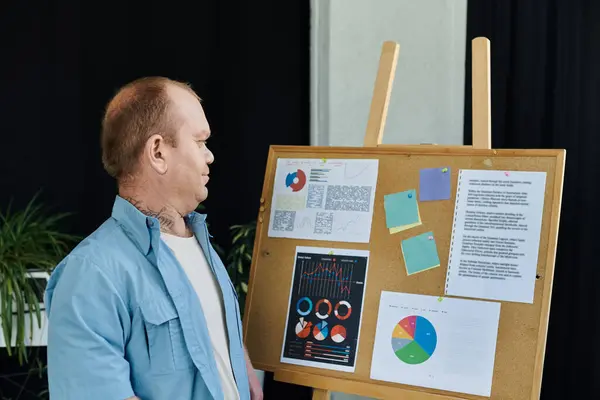 stock image A man with inclusivity stands by a corkboard with charts and papers.