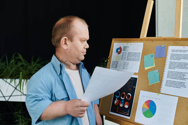 Человек с инклюзивностью стоит перед пробковыми досками, просматривая диаграммы и данные.