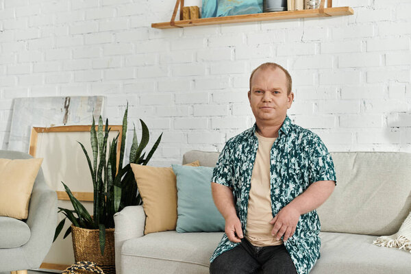 A man with inclusivity in a floral shirt sits on a grey sofa in a modern living room.