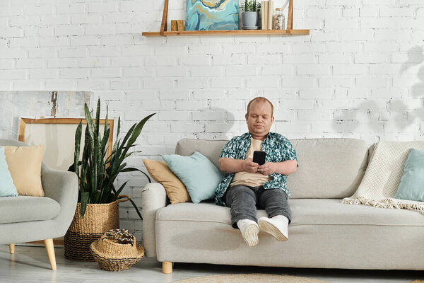 A man with inclusivity sits on a couch in a living room, casually looking at his phone.