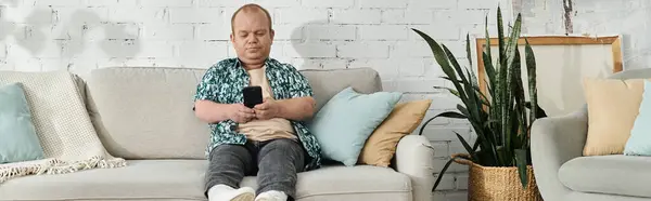 Stock image A man with inclusivity sits on a couch, peacefully scrolling through his phone.