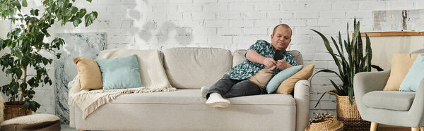 A man with inclusivity is sitting on a white couch in a living room with plants.