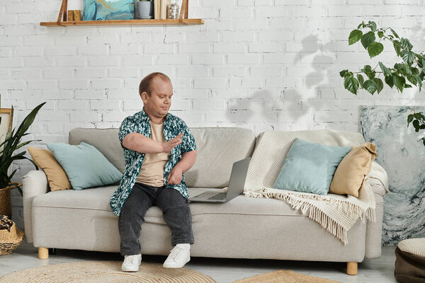 Мужчина с включённостью в голубой рубашке сидит на диване и смотрит помолвленным.